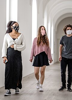 Corona-Pandemie im Museum: Drei Jugendliche auf einem Gang von K21 gemeinsam mit einem Mitarbeiter, der etwas erklärt - alle mit Mundschutz.