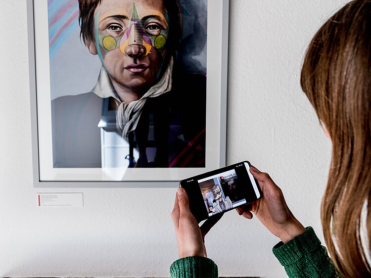 Foto in der Ausstellung; Person von hinten hält ein Smartphone vor einem Porträt Heinrich Heines
