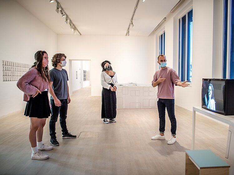 Corona-Pandemie im Museum: Ein Mitarbeiter gibt drei PersonenInformationen zu einem Kunstwerk - Alle mit Mundschutz.