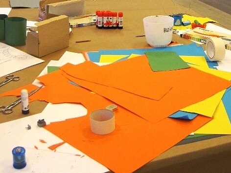 Workshop-Situation: buntes Tonpapier, Klebestifte, Schachteln und Klebeband auf einem Tisch