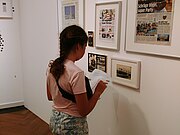 Ein Mädchen steht vor einer Ausstellungswand mit Bildern und löst ein Rätsel