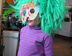 Portrait eines Kindes mit bunter Maske und grüner Perücke.