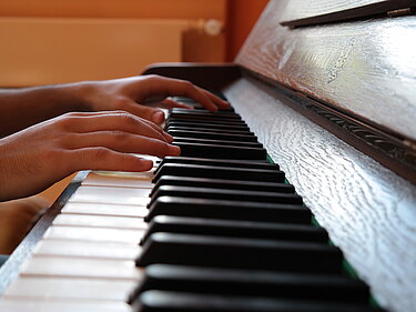 Auf dem Foto ist ein Klavier zu sehen welches von zwei Händen bespielt wird.