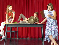 drei Kinder an und auf einem Tisch mit Textblättern, eine Szene übend