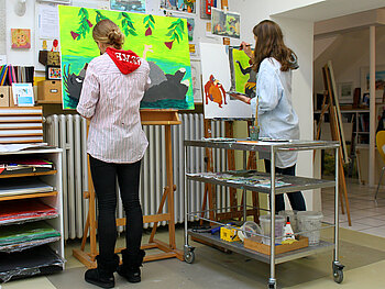 Zwei Jugendliche malen große Acrylbilder an Staffeleien stehend.