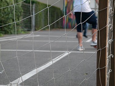 Das Bild ist durch das Netz eines Fußballtores gechossen und bildet fußballspielende Kinder ab.