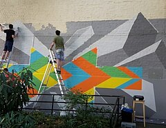 Auf dem Bild ist zu sehen, wie Jugendliche gemeinsam an einem Wandbild arbeiten.