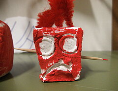 Ein aus Ton gefertigtes kleines eckiges Monster, rot angemalt mit roten Haaren.