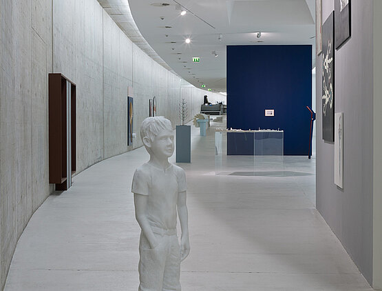 Skulptur eines Jungen mit weiteren Kunstwerken im Hintergrund.