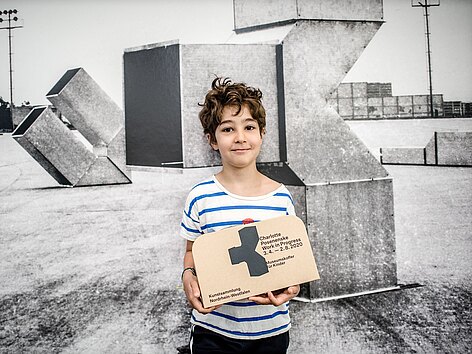 Ein Junge in einer Ausstellung zeigt stolz einen Museumskoffer.