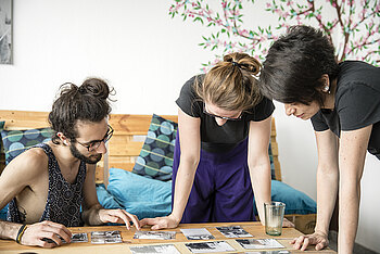 Drei junge Erwachsene betrachten Fotos, die auf einem Tisch liegen