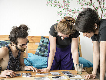 Drei junge Erwachsene betrachten Fotos, die auf einem Tisch liegen
