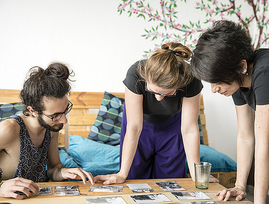 Drei junge Erwachsene schauen sich Fotos auf einem Tisch an