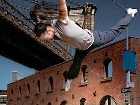 Eine Tänzerin fliegt in der Luft, vor einer urbanen Skyline