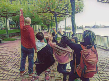 Auf dem Bild ist ein Künstler, ein paar Kinder und eine Frau zu sehen, sie strecken die Hände in die Luft. Sie sind am Düsseldorfer Rheinufer, Platanen säumen den Weg. Rechts ist leicht unscharf der Rhein zu sehen. Das Bild ist im Stil eines Ölgemäldes bearbeitet.
