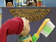 Kasper, mit Zahnbürste bewaffnet, will dem geplagten Wolfram Eckzahn helfen, in der Puppenbühne Bauchkribbeln