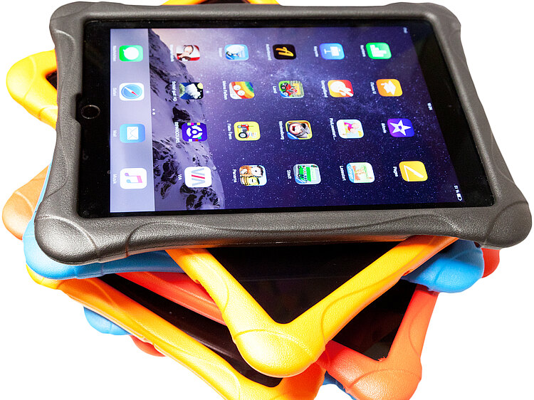 Ein Stapel Tablets in bunten Hüllen, das oberste ist eingeschaltet und zeigt einen Standardstartbildschirm mit App-Symbolen.