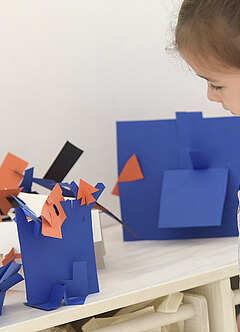 Blaue selbstgemachte Papierfiguren werden von einem kleinen Mädchen bestaunt.