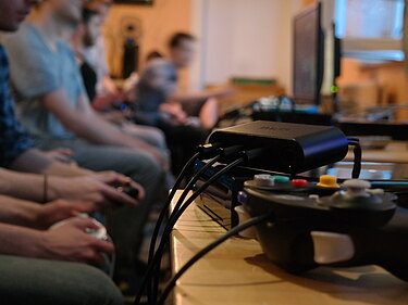 Auf dem Bild sind mehrere Menschen zu sehen welche an Videokonsolen Spiele spielen