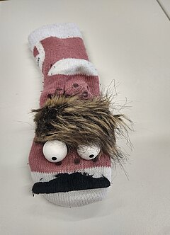 Eine umgestaltete Socke mit Fellhaaren, grimmig dreinblickenden Augen und einem schwarzen Schnäutzer