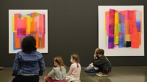 Kinder in einem Museum sitzend vor gemalten abstrakten Bildern