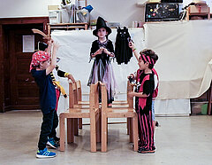 Eine Zauberin steht erhoben auf Stühlen, rechts und links von ihr kleine Piraten, die ihr Schwert in die Höhe halten