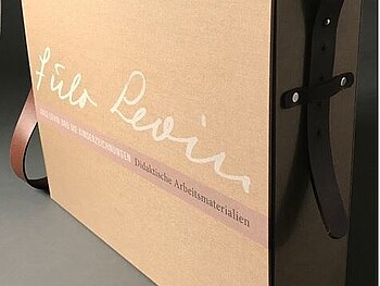 Museumskoffer Julo Levin und die Kinderzeichnungen. Der Koffer erinnert an eine große Aktentasche. Der hellbraune Koffer ist auf der Vorderseite beschriftet. Ein Lederriemen ermöglicht ihn zu tragen.