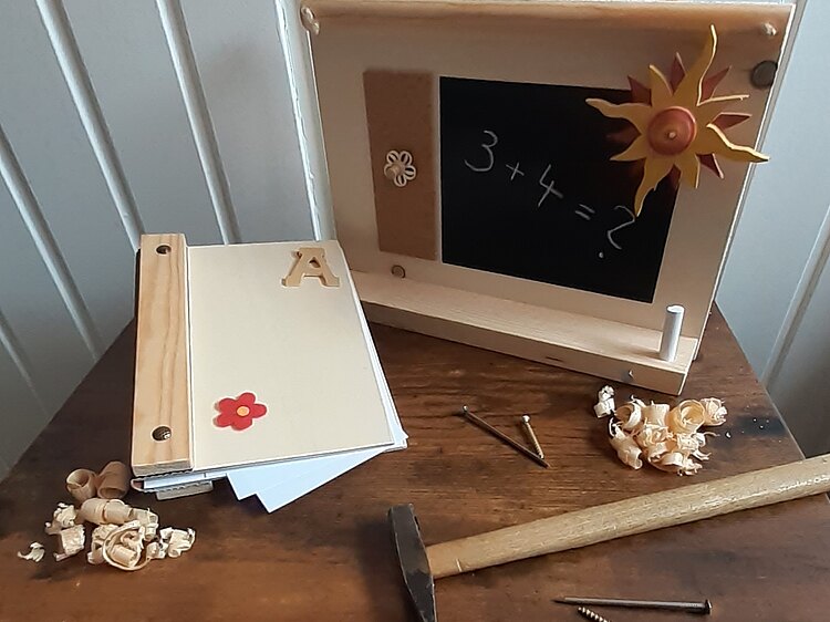 Eine eigene kleine Holztafel mit einer Sonne dekoriert und einer kleinen Halterung für Kreide und ein Buch mit einer Holzeinfassung für eigene kleine Geschichten.