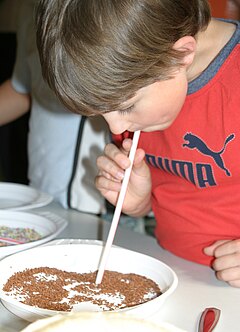 Ein Junge saugt mit einem Strohhalm Schokoladenstreusel von einem Teller.