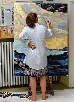 Eine Jugendliche malt an einer Staffelei stehend.