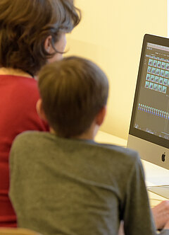 Eine Frau und ein Junge schauen auf einen Bildschirm in der Medienwerkstatt von K21.