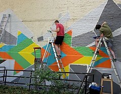 Auf dem Foto ist zu sehen, wie Jugendliche gemeinsam an einem Wandbild arbeiten.