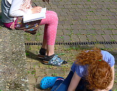 zwei Kinder in der Sonne auf einem Schulhof sitzend und konzentriert schreibend