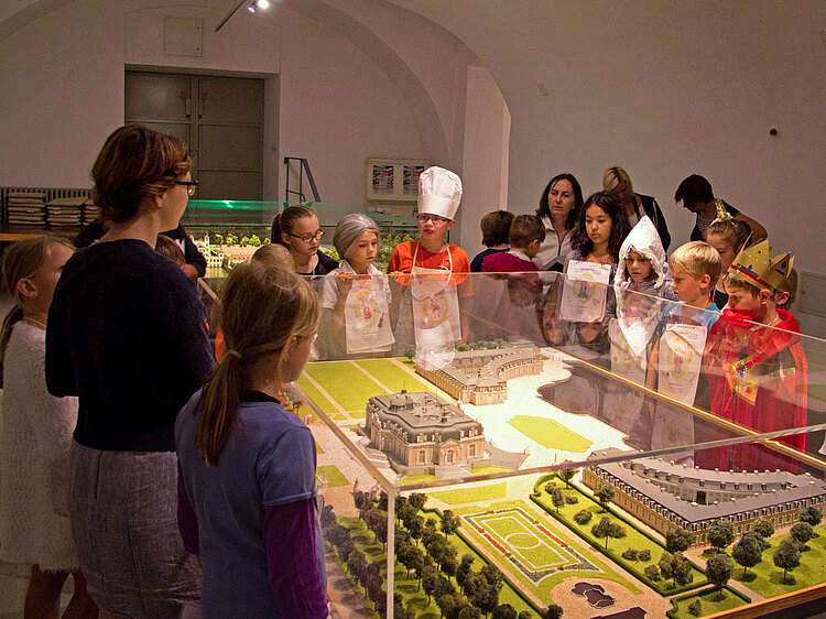 Eine Gruppe von Kindern steht gemeinsam um eine Miniatur Nachbildung des Schlosses herum.