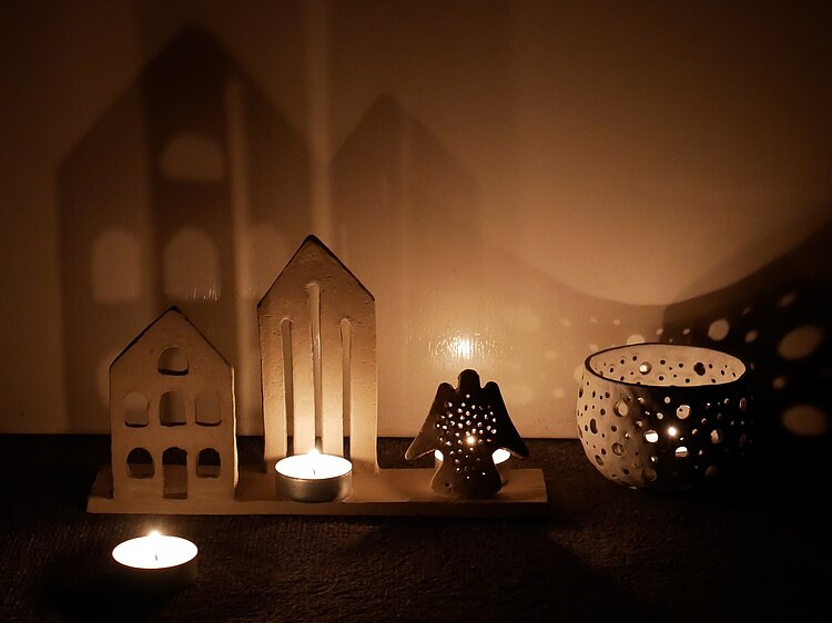 Eine Hausfassade, eine Kirchenfassade, ein Engel und eine Schale mit Löchern. Alle dienen als Kerzenhalter.