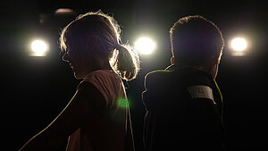 Mädchen und Junge stehen auf einer dunklen Bühne im Gegenlicht