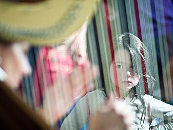 Kind sitzt staunend hinter einer Harfe.